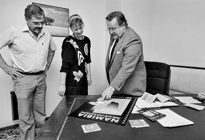 YK:n Namibian-erityisedustaja Martti Ahtisaari ensimmäistä päivää toimessaan Windhoekissa Namibiassa 1. huhtikuuta 1989. Ahtisaari, hänen apulaisensa Cedric Thornberry ja YK:n PR- ja julkaisupäällikkö, norjalainen Jan Anderssen esittelevät vaalijulistetta "Namibia Free and Fair Elections" .
